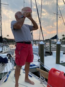 sailor blowing a conch horn on the bow of his sailboat