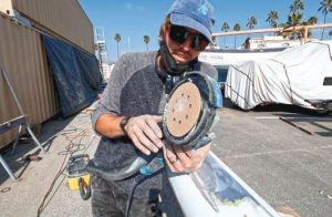The author's husband, Chris, uses an angle grinder with a5-inch hook-and-loop sanding pad to remove the mast’s
old paint.