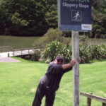 Picture of someone leaning on a slippery slope sign