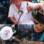 Two simple tools, a basin wrench and a belt-tensioning jack, top left, are Jim’s “friends in low places” that enable him to deal with two maintenance demons that lurk in impossible places under and behind his V-drive-equipped engine. Armed with these tools, top right, he has a fair chance when reaching under the engine block to adjust the stuffing box or when setting the accessory-belt tension. The belt-tensioning jack holds the present setting while Jim makes the adjustment, above. In addition, it provides a valuable extra hand where there is no room for a human one.