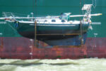 A boat hanging from a giant crane off the side of a container ship