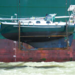 A boat hanging from a giant crane off the side of a container ship