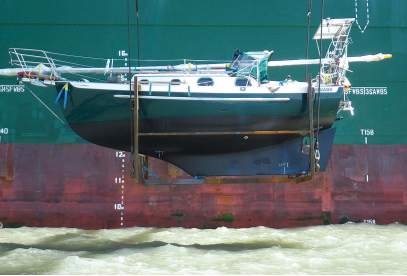 A boat hanging from a giant crane off the side of a container ship