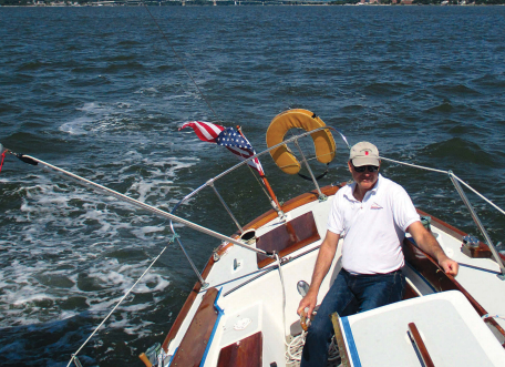 John chooses the simplicity of a tiller, at left, (here in his brother Charlie’s hand) over the complexity of wheel steering. John generally sails alone or with one other so the tiller presents no problems as it might with a larger crew. At anchor, the tiller is stored vertically so it is completely out of the way.
