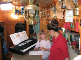 Danielle gives Antigone a piano lesson under the big kerosene lamp. It was later sold as the light from four smaller bulkhead lamps was sufficient.