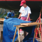 A woman sewing by a boat