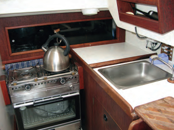 A gimbaled two-burner stove/oven, a sink, and a small countertop make up the starboard side of the compact galley. An icebox and counter are to port. Jerry built a cutting board that slips over the top companionway step.