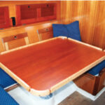With a couple of modifications, Joe increased the utility of the dinette table in his Bristol 30. Turned fore and aft and slid outboard, it opens up space in the saloon, at left on facing page. In its central position, it serves as a dining table for four, at right on facing page. Turned through 90 degrees, it can be slid forward or aft to meet a variety of uses, at left.