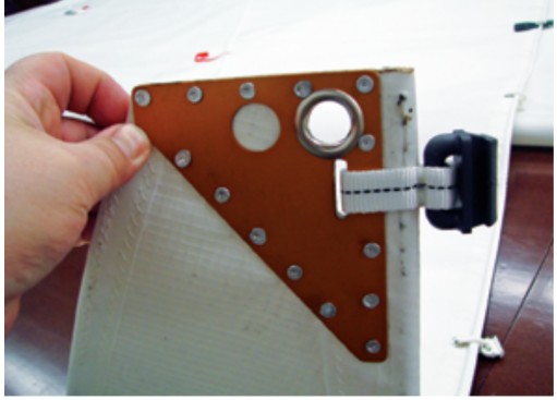 Installing the hardware, such as the mainsail headboard and slide shown here, involves a great deal of handwork. Nearly all of this work can be done with inexpensive tools, sail twine and webbing, and soft aluminum rivets.