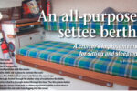The Reids’ three-in-one berth in its settee configuration with the removable fiddle set in place to restrain the cushion. The fiddle’s short steel rods fit into the eye straps through-bolted through the darker strip of teak below the fiddle, which itself is through-bolted through the liner. The thin plates below the eye straps serve both as shims to prevent wobble and strakes to prevent the rod ends from digging into the wood.