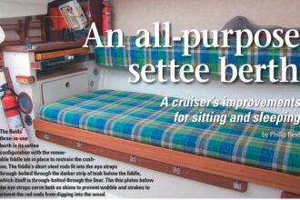 The Reids’ three-in-one berth in its settee configuration with the removable fiddle set in place to restrain the cushion. The fiddle’s short steel rods fit into the eye straps through-bolted through the darker strip of teak below the fiddle, which itself is through-bolted through the liner. The thin plates below the eye straps serve both as shims to prevent wobble and strakes to prevent the rod ends from digging into the wood.