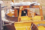 The Old Cat at her dock, furled sail on the boom gallows. Note the boarding steps on the rudder and transom.