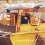The Old Cat at her dock, furled sail on the boom gallows. Note the boarding steps on the rudder and transom.