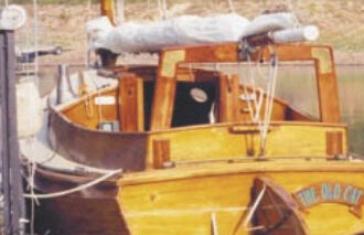 The Old Cat at her dock, furled sail on the boom gallows. Note the boarding steps on the rudder and transom.