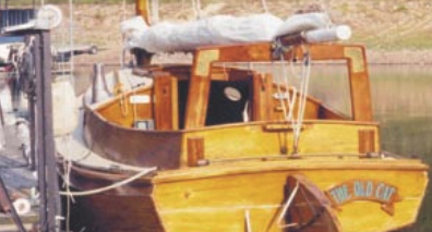 The Old Cat at her dock, furled sail on the boom gallows. Note the boarding steps on the rudder and transom.