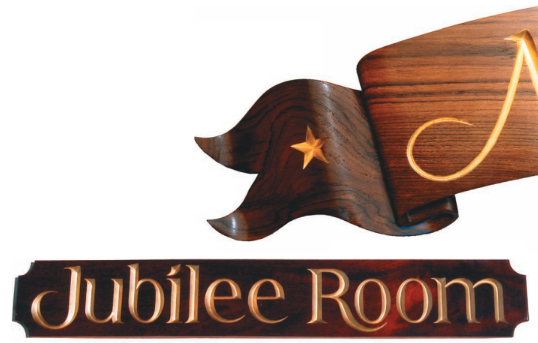 The “wings” of the nameboard, at right, can be carved to achieve a windblown effect. Note how the wing appears to fold behind the main board. Paul carved the Jubilee Room board, below, to identify his yacht club’s party/meeting room. The letter style came from Rosemary Sassoon’s book.