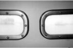 John Karklins’ finished portlights above. He recommends against using polycarbonate. It gets cloudy, as the illustration shows. The teak spacer he added to compensate for the additional thickness of his “armor-plated windows” shows around the edges of the frame.
