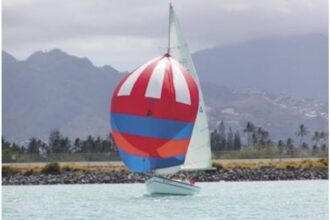 The Rhodes 19, christened in 1971 by group members as Wet Hen, glides across a Honolulu backdrop.
