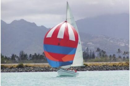 The Rhodes 19, christened in 1971 by group members as Wet Hen, glides across a Honolulu backdrop.