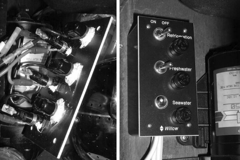 At left, the back side of the new electrical panel. The switches are in the foreground, and the fuse holders are in the background. The white goop on the switches is marine urethane sealant. The fuse holders also have a dab of marine urethane sealant to keep the nuts from loosening. The finished sub-panel installed under the galley sink, at right. All the wires lead into and out of the box on the bottom.