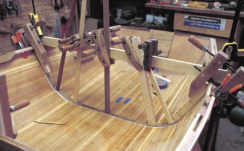 Installing the rib, at left, using a steamed piece of teak bedded down with epoxy glue then covered with a strip of fiberglass cloth. This will help keep the hull from twisting when the dinghy is rowed.