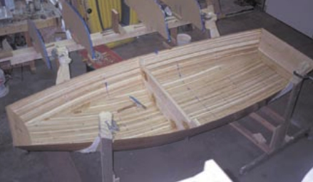 The unglassed inside of the boat, at right, connected together and ready for sanding. Sanding the inside is the hardest part of building this boat, John says. Next the sanded hull is dusted and cleaned with acetone and a reinforcing layer of fiberglass cloth is added to the bow and transom. “On the first boat,” John says, “We put the reinforcing cloth on after the overall boat was glassed. I did it the other way the next time. Smooth the cloth out as best you can before you wet it down with epoxy,” John suggests. “The flatter you get it to lie here, the less you have to sand later. Unfortunately I did not take a picture of the whole boat covered in glass, which should go on as one piece.” Once the boat is covered with glass, use a squeegee to apply the thick epoxy resin. Wet the glass thoroughly with the resin and carefully scrape it down. Get a friend to help mix the resin, which hardens quite rapidly. Once you start this part, you need to finish. Doing a careful job here will save sanding time later. It takes three coats of epoxy to fill in the weave of the cloth and leave a smooth hull. The inside gets only two coats to leave a rougher surface for traction.