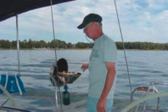 A member of the Tuesday-evening racing crew, Dave Michalkiewicz, uses the grill on Another Adventure, author Barry Hammerberg’s 1990 Hunter Legend 35.5. The propane bottle is stored on the stern pulpit in a mesh bag.
