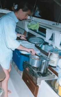On their frequent cruises Trish cooks aboard using their non-pressurized alcohol stove. They use the built-in icebox (foreground) as a cupboard, and store chilled foods in a standard portable cooler (on the settee).