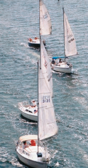 The C-22 fleet sails under the bridge connecting Navarre and Navarre Beach, Fla., during the 2000 Annual Northern Gulf Cruise. This year’s cruise is planned for May12–18. The Endicotts sail #12759, the white hulled sloop with the blue Bimini.