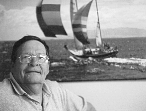 Edward (“Ted”) Brewer poses in his office with a picture of one of his early designs, the 53-foot aluminum ketch, Mystic, on her way to taking second in Class B in the Trans-Pac. The lines for Black Velvet, one of his favorite designs, are at left.